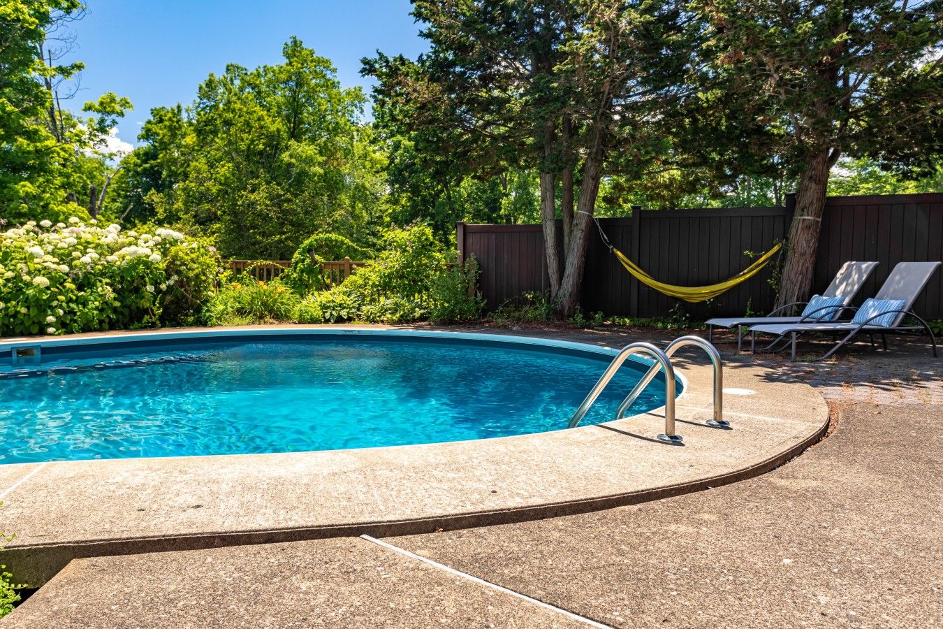 A swimming pool with a metal ladder, surrounded by a wooden fence and trees.