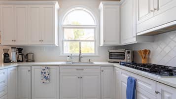 A kitchen with white cabinets, a window, a stove, and a coffee maker.