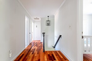A hallway with wooden flooring, white walls, and a black railing.