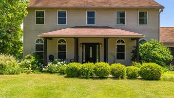 A two-story house with a covered porch, a front door, and a small garden with bushes and flowers.