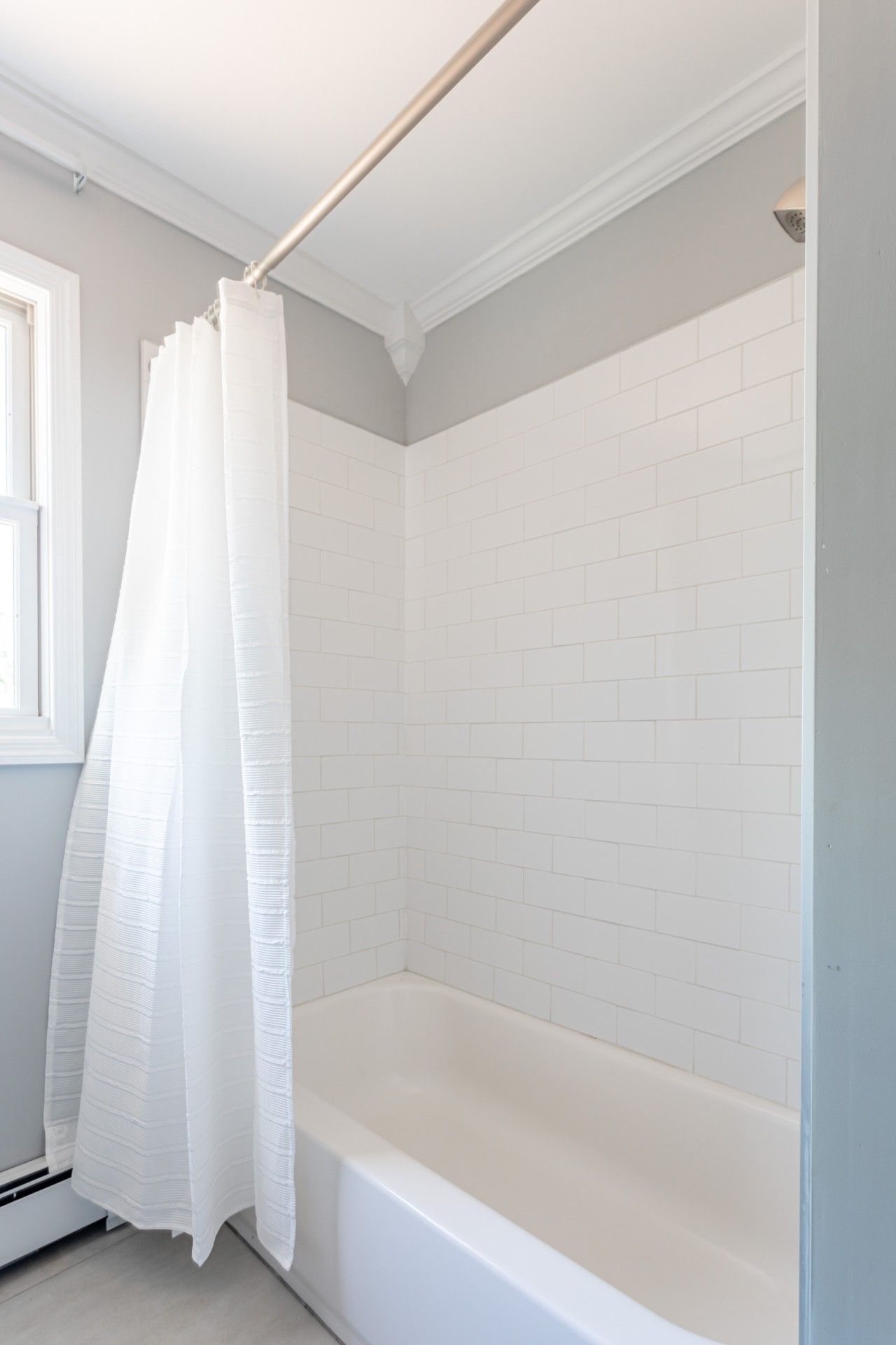A bathroom with white tiled walls, a white bathtub, and a white shower curtain.