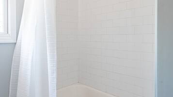 A bathroom with white tiled walls, a white bathtub, and a white shower curtain.