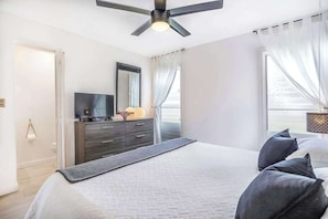 Ein Hotelzimmer mit Bett, Fernseher, Schminktisch und Deckenventilator.