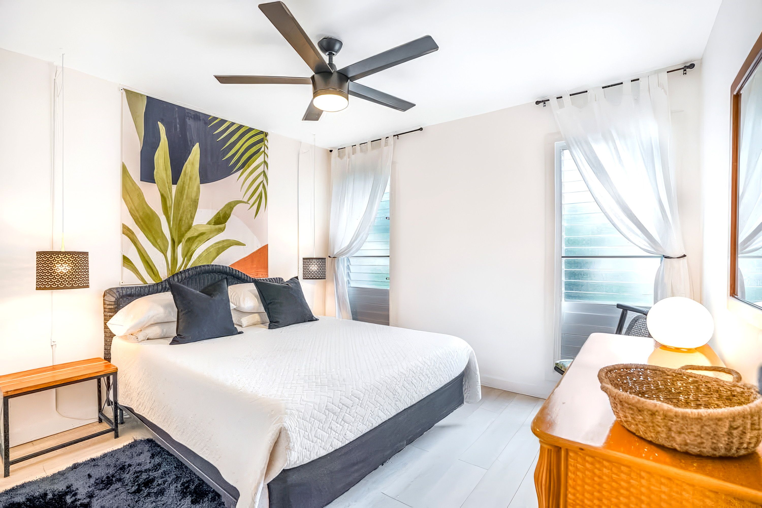 A modern bedroom with a bed, a ceiling fan, a large window with curtains, and a bedside table with a lamp.