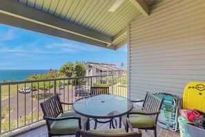 A balcony with a round table and chairs, a yellow water container, and a view of the ocean and buildings. - *New* Top-Floor Princeville Views for Family Time (Princeville)