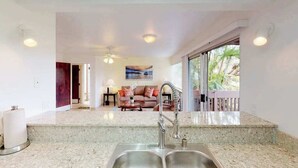 Eine Küche mit doppeltem Spülbecken, einem Deckenventilator und Blick auf ein Wohnzimmer mit Sofa und Gemälde.