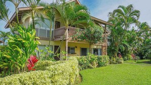 Ein zweistöckiges Gebäude mit einem Balkon, umgeben von üppiger Vegetation und Palmen.