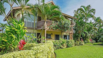 A two-story building with a balcony, surrounded by lush greenery and palm trees.