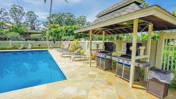 A swimming pool with lounge chairs, a barbecue grill, and a covered pavilion.