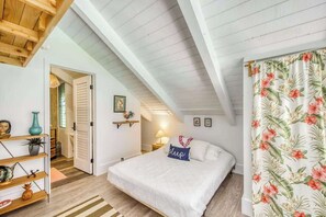 Ein Schlafzimmer mit schrägen Wänden, einem Bett mit weißer Bettdecke, einem blumigen Vorhang und einem Regal mit Dekoration.