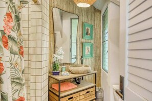 Ein Badezimmer mit einem Holzlagerfläschchen, einem großen Spiegel und einem Fenster mit Jalousien.