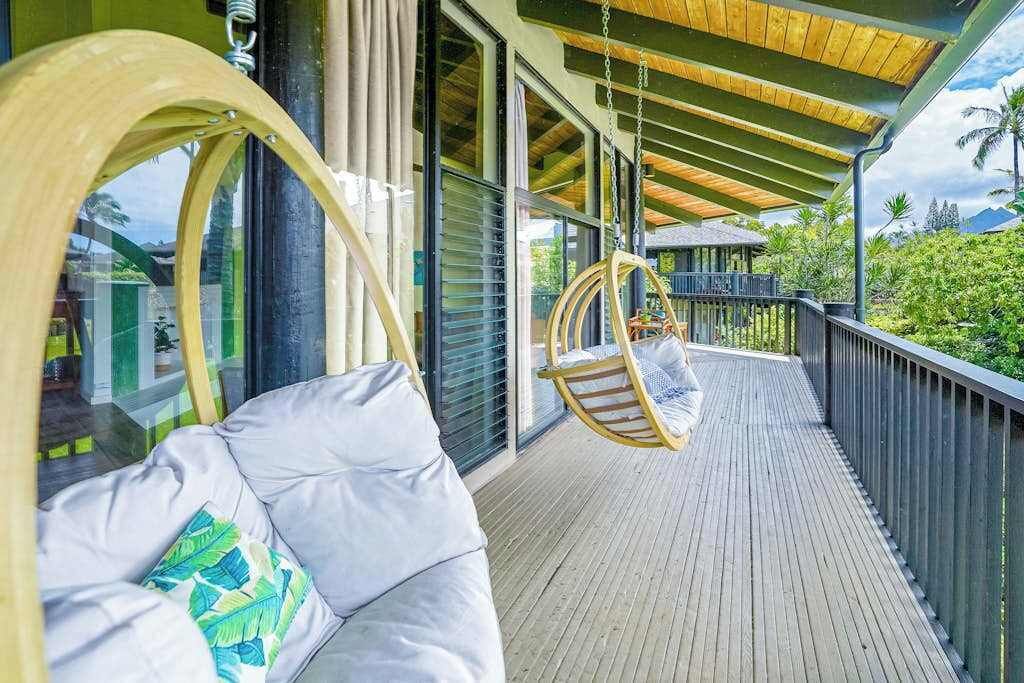 A wooden deck with a hanging chair and a cushioned seating area.