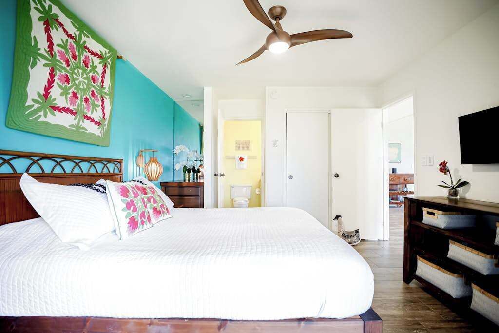 A bedroom with a bed, a ceiling fan, a TV, and a door leading to another room.