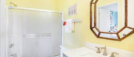 A bathroom with a glass shower enclosure, a toilet, a sink with a mirror, and a towel rack.