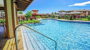 Una piscina amb terrassa enrajolada i baranes metàl·liques, envoltada de vegetació abundant i edificis residencials.