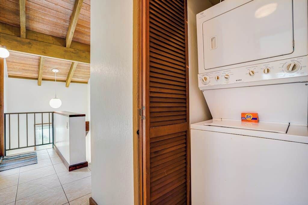 A laundry room with a white washing machine, wooden slatted door, and a small box of Tide detergent on top.