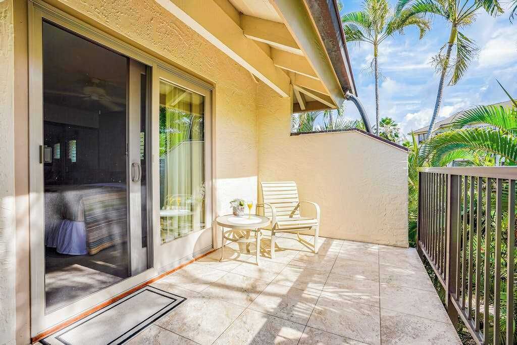 A balcony with a sliding glass door, a small table with a chair, and a view of palm trees.