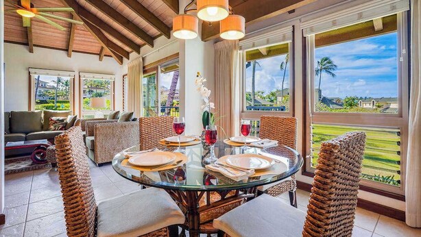 Uma área de jantar com mesa de vidro, cadeiras de vime e vista para um campo de golfe.