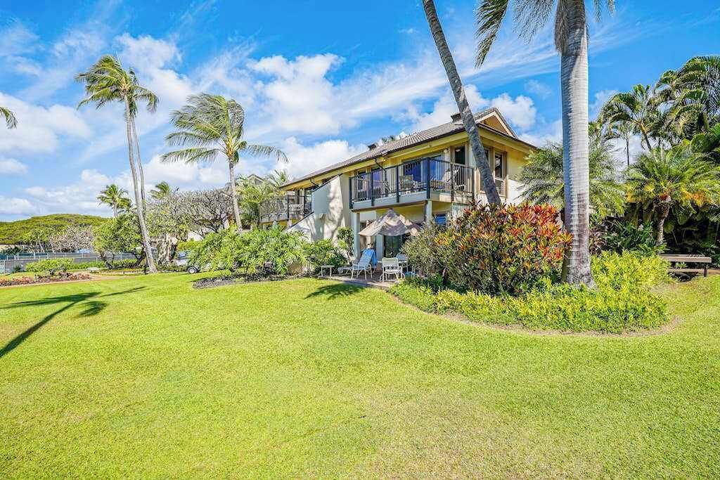 A two-story building with a balcony, surrounded by a well-maintained lawn and palm trees.