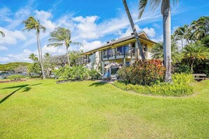 A two-story building with a balcony, surrounded by a well-maintained lawn and palm trees. - New Top-Floor Poipu Corner Condo With Two Lanais (Koloa)