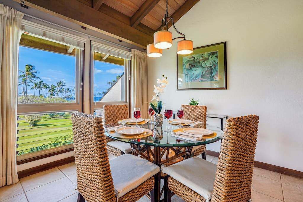 Een eethoek met rieten stoelen, een glazen tafel en uitzicht op palmbomen.