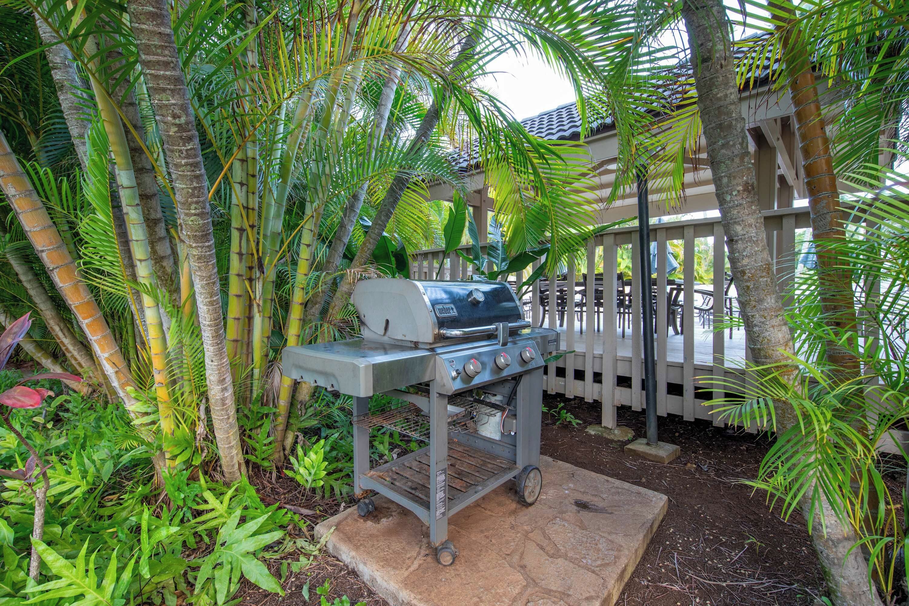 An outdoor grill area with a barbecue grill, surrounded by lush greenery and a wooden deck.