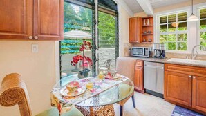 Eine Küche mit Holzschränken, einem Glastisch mit Blumenmuster-Tischdecke und Blick ins Grüne.
