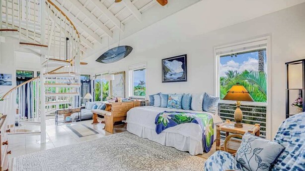 A spacious bedroom with a large bed, a desk, a chair, and a view of the outdoors. - NEW Corner Princeville Loft Studio with Hanalei Mountain Views (Princeville)