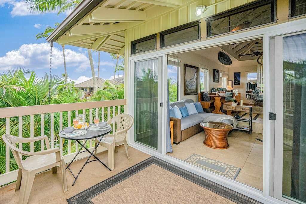 Een overdekt balkon met een tafel en stoelen, een bank en een keukenruimte zichtbaar door glazen deuren.