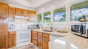 A kitchen with wooden cabinets, a white stove, a sink, and a window with a view of palm trees. - NEW Corner Princeville Loft Studio with Hanalei Mountain Views (Princeville)