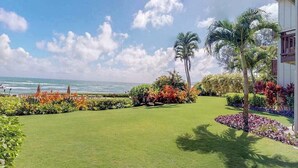 A well-maintained lawn with a view of the ocean, palm trees, and a building with a balcony. - *NEW* Oceanfront Wailua Days at Lanikai, Steps from Lae Nani (Kapaa)
