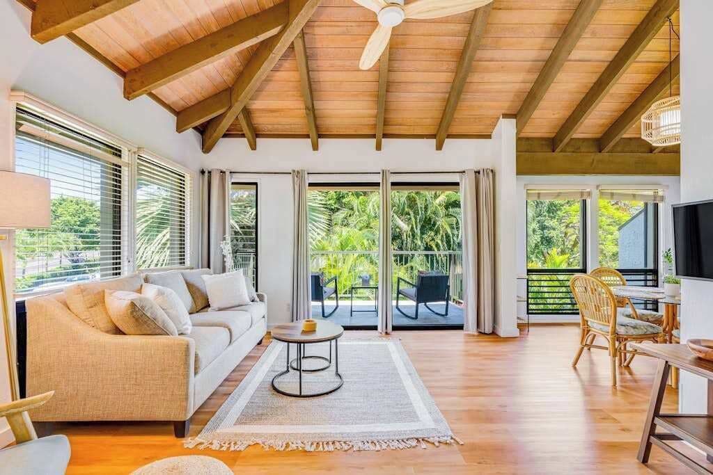 A spacious living area with a wooden ceiling, a sofa, a coffee table, and a balcony with outdoor furniture.