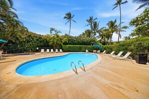 Ein Pool mit geschwungener Kante, umgeben von Liegestühlen und Palmen.