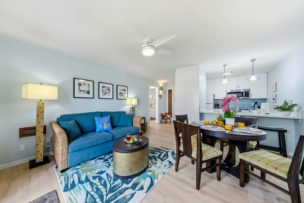 Ein modernes Wohnzimmer mit einem blauen Sofa, einem runden Couchtisch und einer Essecke für zwei Personen.