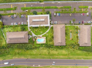 An aerial view of a property with a swimming pool, multiple parking spaces, and a road with vehicles. - *NEW* Fall $pecial Beachside Kapaa Condo with Three Pools and Hot Tubs (Kapaa)