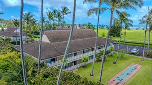 A two-story building with a flat roof, surrounded by palm trees and a parking lot. - *NEW* Fall $pecial Beachside Kapaa Condo with Three Pools and Hot Tubs (Kapaa)