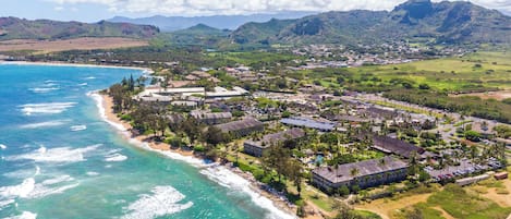 Resort costeiro com villas na praia, piscina e vista para o oceano e montanhas.