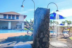 A pool area with a stone pillar, lounge chairs, and a building in the background. - Custom Poipu Home on Kiahuna Golf w/ Poipu Beach Athletic Club Pool & Courts (Koloa)