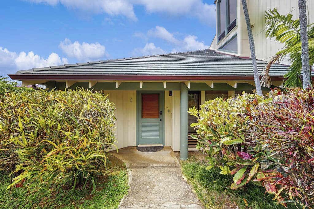 A house with a front porch, a door, and a small garden area with various plants.