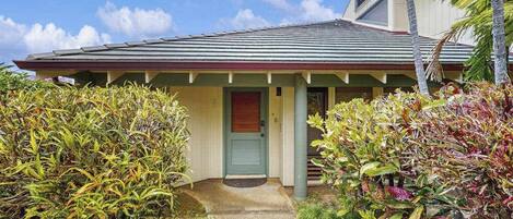 A house with a front porch, a door, and a small garden area with various plants.