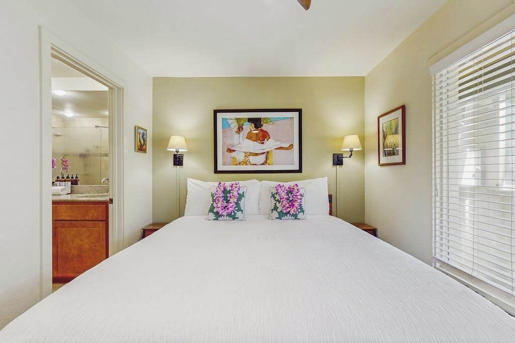 A hotel room with a bed, two bedside lamps, a painting on the wall, and a window with blinds.