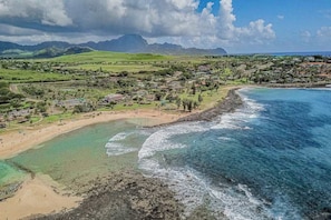 Uma vila costeira com uma praia, águas cristalinas e montanhas ao fundo.
