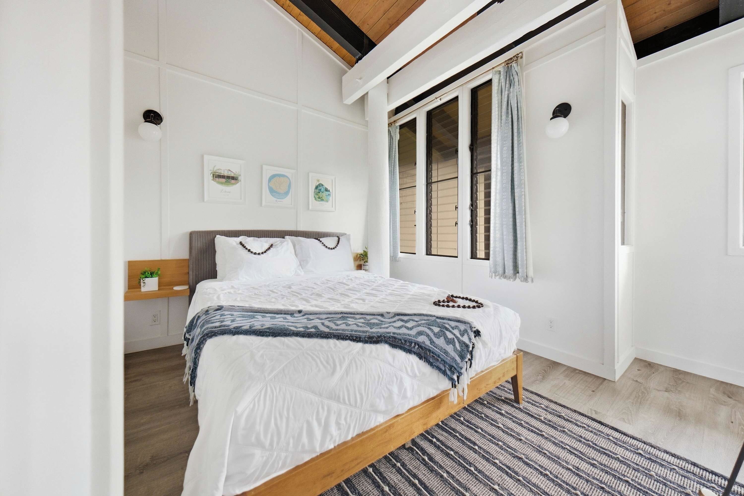 A bedroom with a bed, a nightstand, a window with curtains, and wall art.