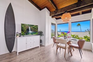 A modern kitchen with a large flat-screen TV, wooden cabinets, and a dining area with a table and chairs. - Hanalei Bay Mauna Kai 5- Pool, Kitchen, Beach Gear, WIFI, W/D, Family Friendly (Princeville)