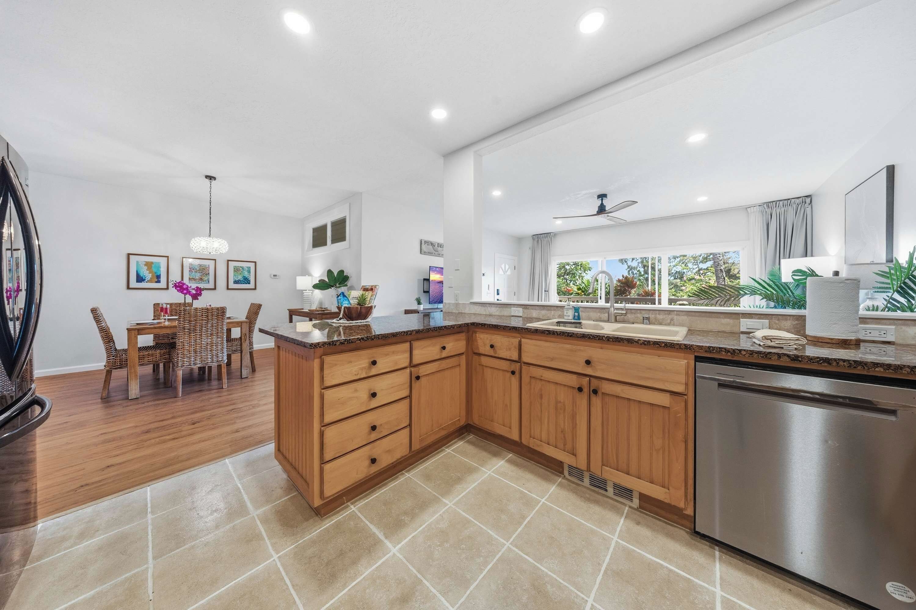 A modern kitchen with wooden cabinets, a stainless steel dishwasher, and a dining area with wicker furniture.