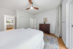 A bedroom with a bed, a dresser, a ceiling fan, and a door leading to another room. - Poipu Mermaid Family Condo - Pool, Hot Tub, Tennis, AC, Kitchen, Laundry, Beach (Koloa)