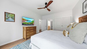 Una camera da letto con un letto, una televisione, un ventilatore a soffitto, un comò e una porta che dà su un'altra stanza.