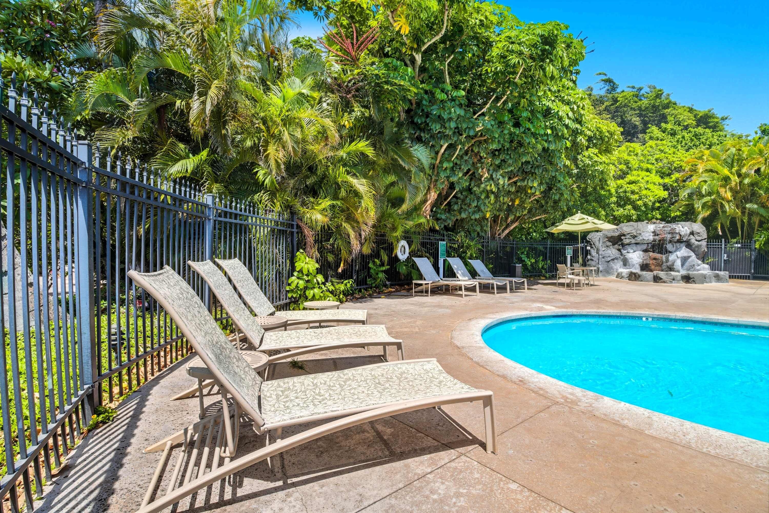 Un área de piscina con sillones de descanso y una piscina azul cristalina.