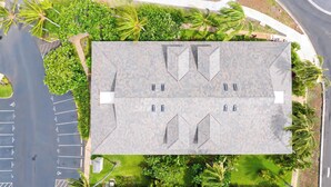 Un edificio con tetto piano, diverse finestre, circondato da vegetazione e un'area di parcheggio.