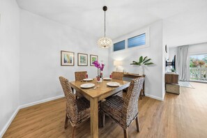 A dining area with a wooden table, wicker chairs, and a hanging light fixture. - Poipu Mermaid Family Condo - Pool, Hot Tub, Tennis, AC, Kitchen, Laundry, Beach (Koloa)